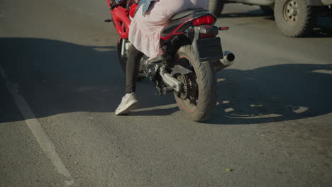 two ladies riding a power bike on a tarred road as they slow down in traffic, the rider places her left leg down for balance and support while moving forward