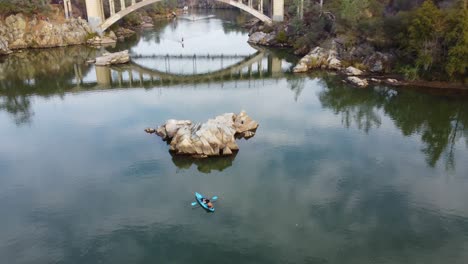 traveling drone footage of still reflective water with a bridge in the background, focusing in on lone kayaker