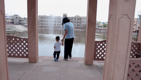 young mother holding toddler son finger and walking at outdoor at evening