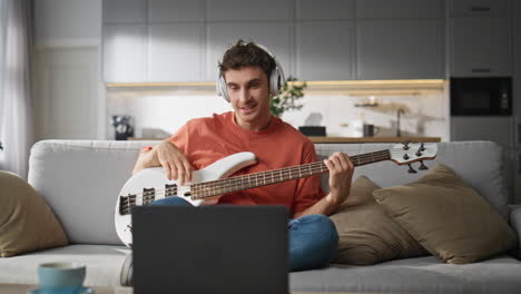 talented man playing guitar at sofa. handsome guy in headphones reading chords