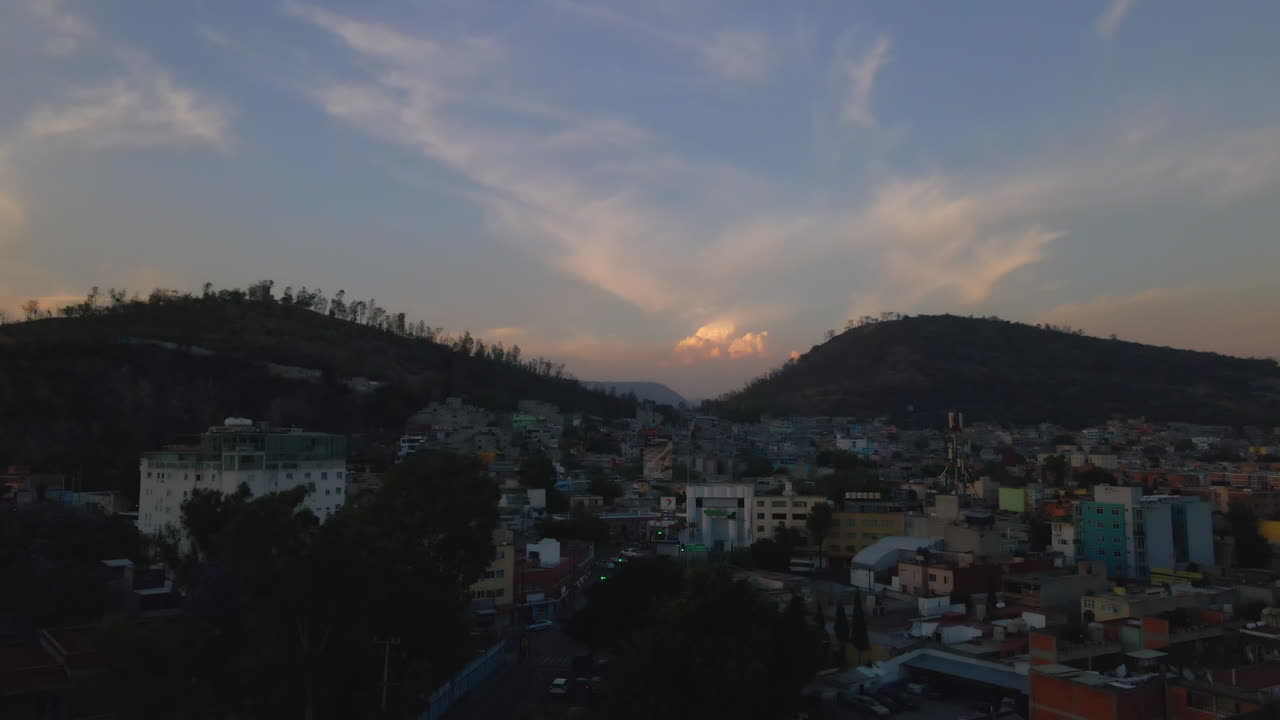 vista aérea ascendente de edificios de apartamentos y casas en una zona residencial rodeada de colinas y naturaleza al atardecer