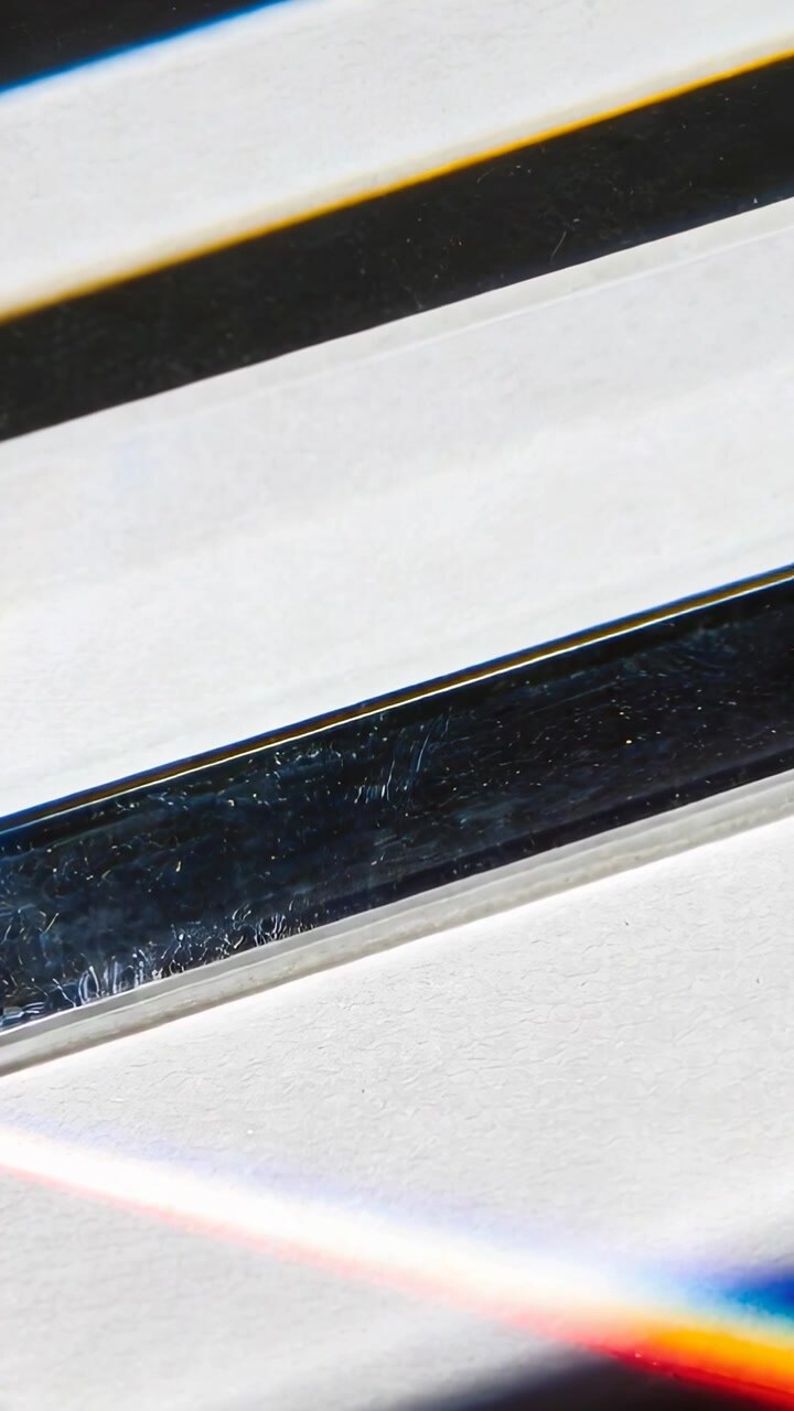 Video verticale: Striscia metallica in movimento che mostra un luccichio con luce che scivola su una superficie bianca, arcobaleno.