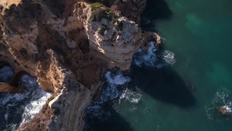 Top down aerial of rough textured and eroded Mediterranean cliffs. waves swirl in the turquoise sea.