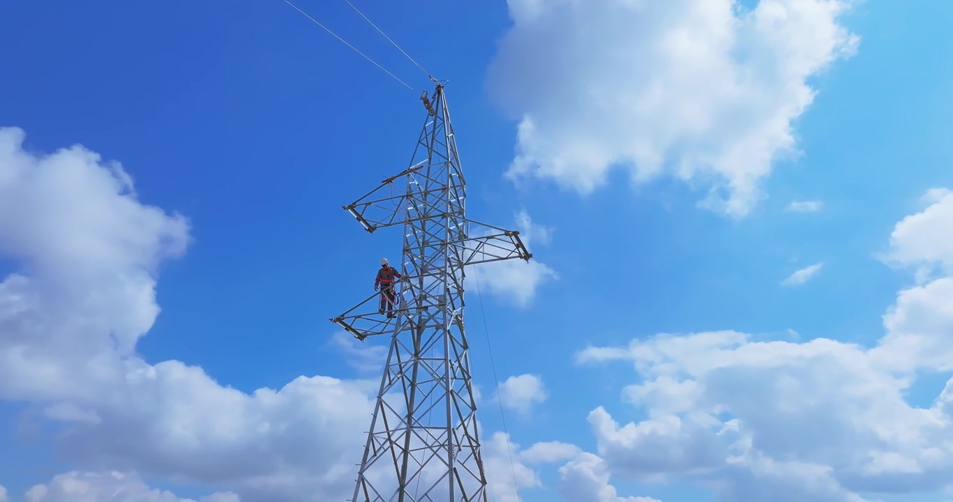 Electrical line technician working on a steel lattice transmission tower with ground maintenance crew and service vehicles below near Santo Antônio do Monte, Minas Gerais, Brazil, drone orbit descent