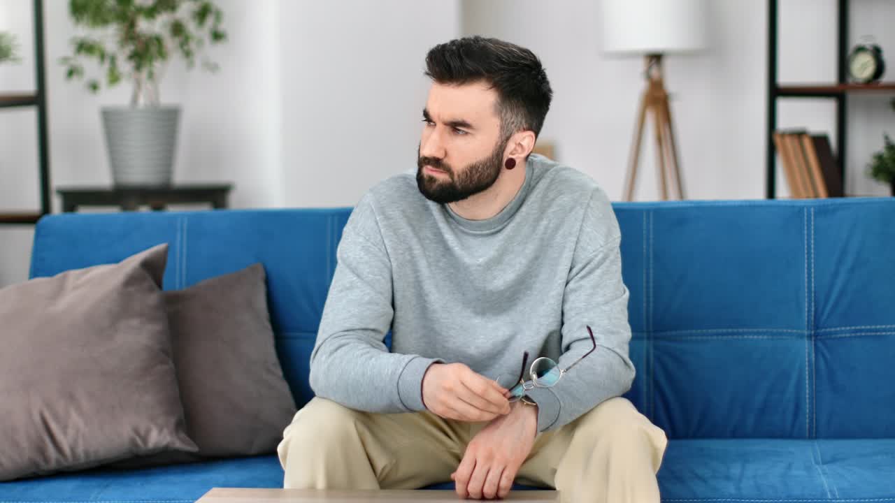 Uomo hipster casual turbato per un tradimento, con problemi di relazione e che soffre di solitudine, seduto sul divano