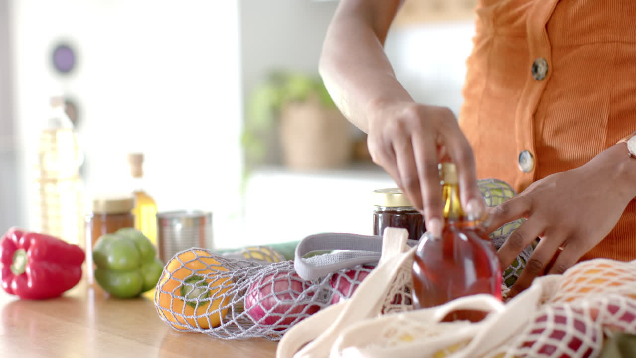 Placing groceries on kitchen counter, woman unpacking fresh vegetables and jars