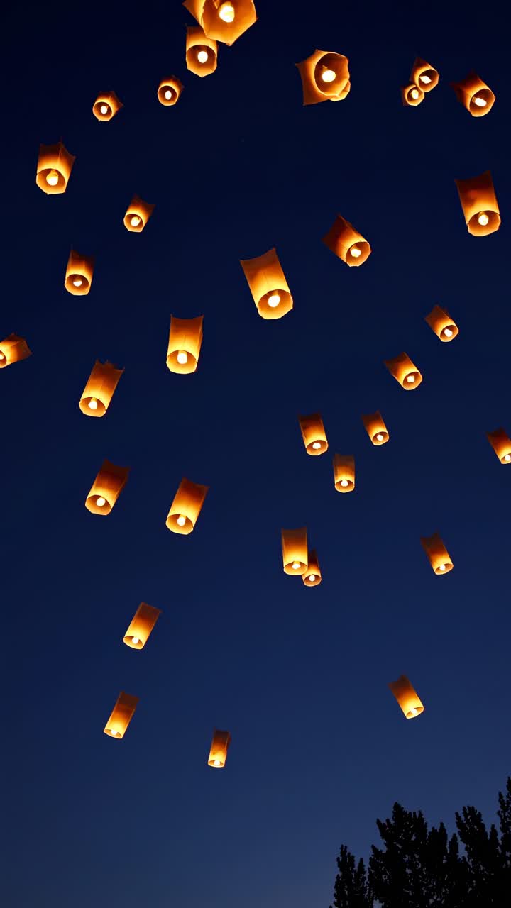 A mesmerizing video still of glowing lanterns ascending into a deep blue sky