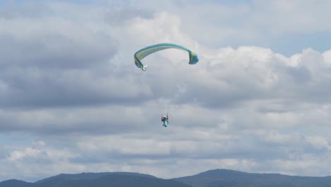 Persona-Volando-En-Parapente-Sobre-Una-Montaña-Boscosa-Con-Nubes-Blancas-En-El-Fondo---Mirador-De-Colofonias-En-El-Borde-Panorámico,-Qld,-Australia