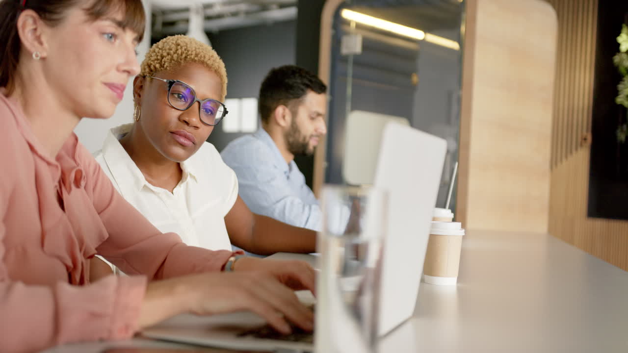 Collaborating on project, diverse colleagues discussing work and using laptops in office