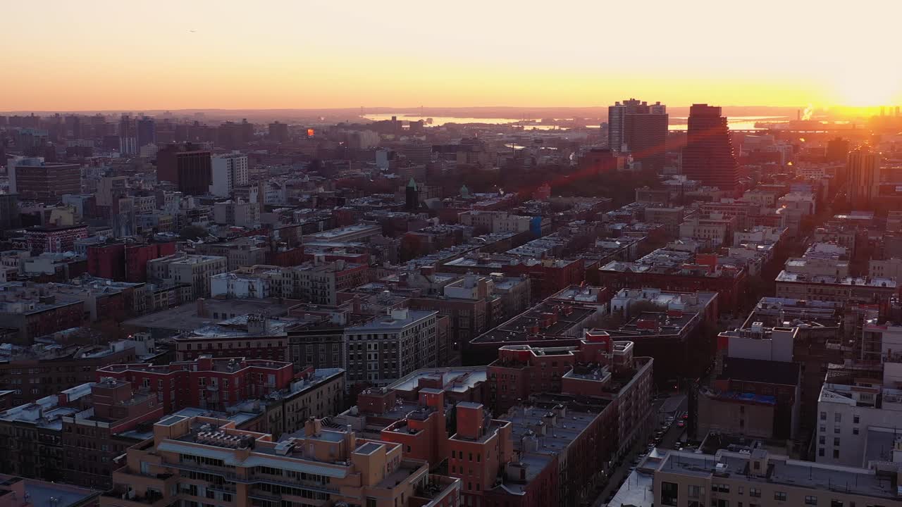 Dramatic aerial upward tilting pan across New York City's Harlem neighborhood at golden hour sunrise with small lens flare