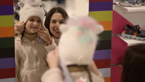 Mother-and-daughter-try-on-cute-winter-hat-in-front-of-the-mirror