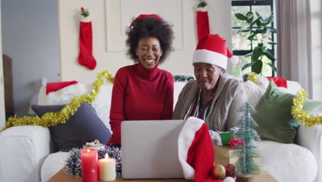 Feliz-Madre-Afroamericana-E-Hija-Adulta-Con-Sombreros-De-Santa-En-Videollamada-Navideña,-Cámara-Lenta