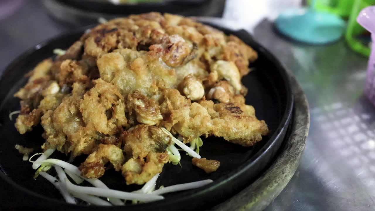 Golden oyster pancake on sizzling pan, vibrant street food setting, shallow depth, evening lighting