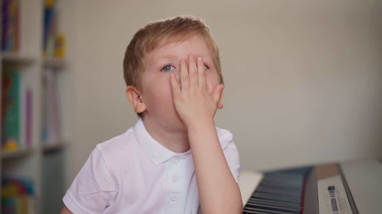 Bambino curioso si lecca il palmo e guarda la mano vicino al pianoforte