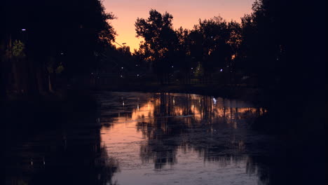 The-beautiful-sunset-view-of-a-canal-filled-with-moss-flowing-under-the-bridge-in-the-peaceful-city-of-Leiria,-Portugal---Wide-shot