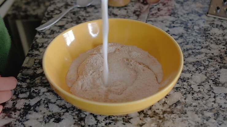 Donna che versa il latte sugli ingredienti secchi in una ciotola per formare una pastella.