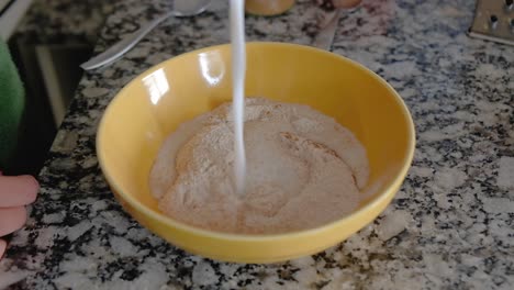 woman pouring milk over dry ingredients on a bowl to form a batter