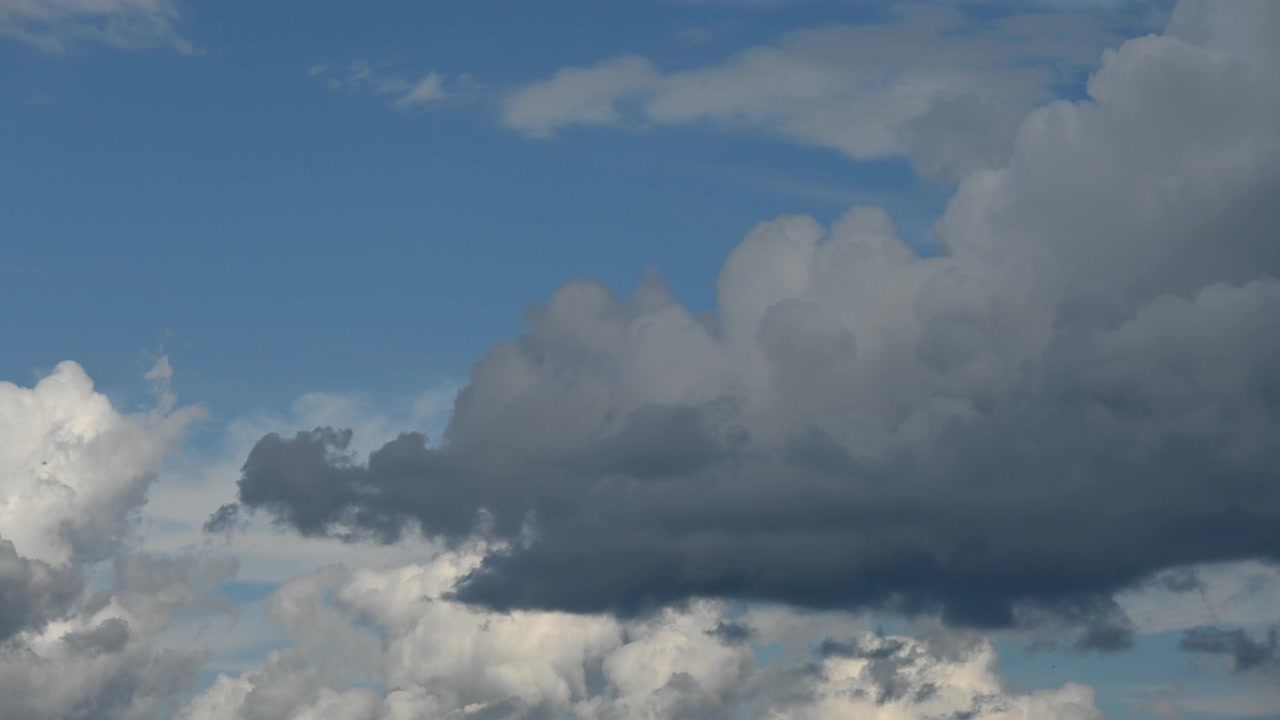 Dark and white clouds create a dramatic contrast against a bright blue sky, suggesting impending weather changes.