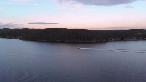 Drone-pan-of-motorboat-speeding-along-coastline-during-golden-hour