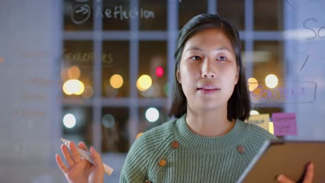 asian casual businesswoman using tablet presenting to colleagues at night in office