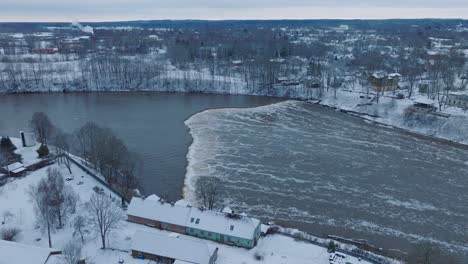 Aerial-establishing-view-of-Venta-river-rapids-during-winter-flood,-Kuldiga,-Latvia,-overcast-winter-day,-wide-drone-shot-moving-forward-tilt-down