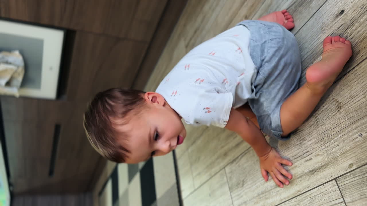 Caucasian baby boy sitting on the floor. Kid jumps up and runs to the toy car and sits on it. Vertical view.