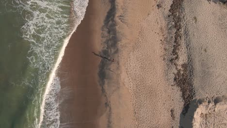 Luftdrohnenaufnahme-Einer-Person,-Die-Mit-Langen-Schatten-Am-Strand-Läuft