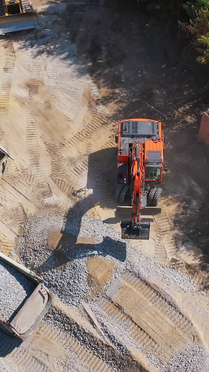 View from above on excavator and two trucks. Excavator working near the machinery with granite stones. Aerial view. Vertical video