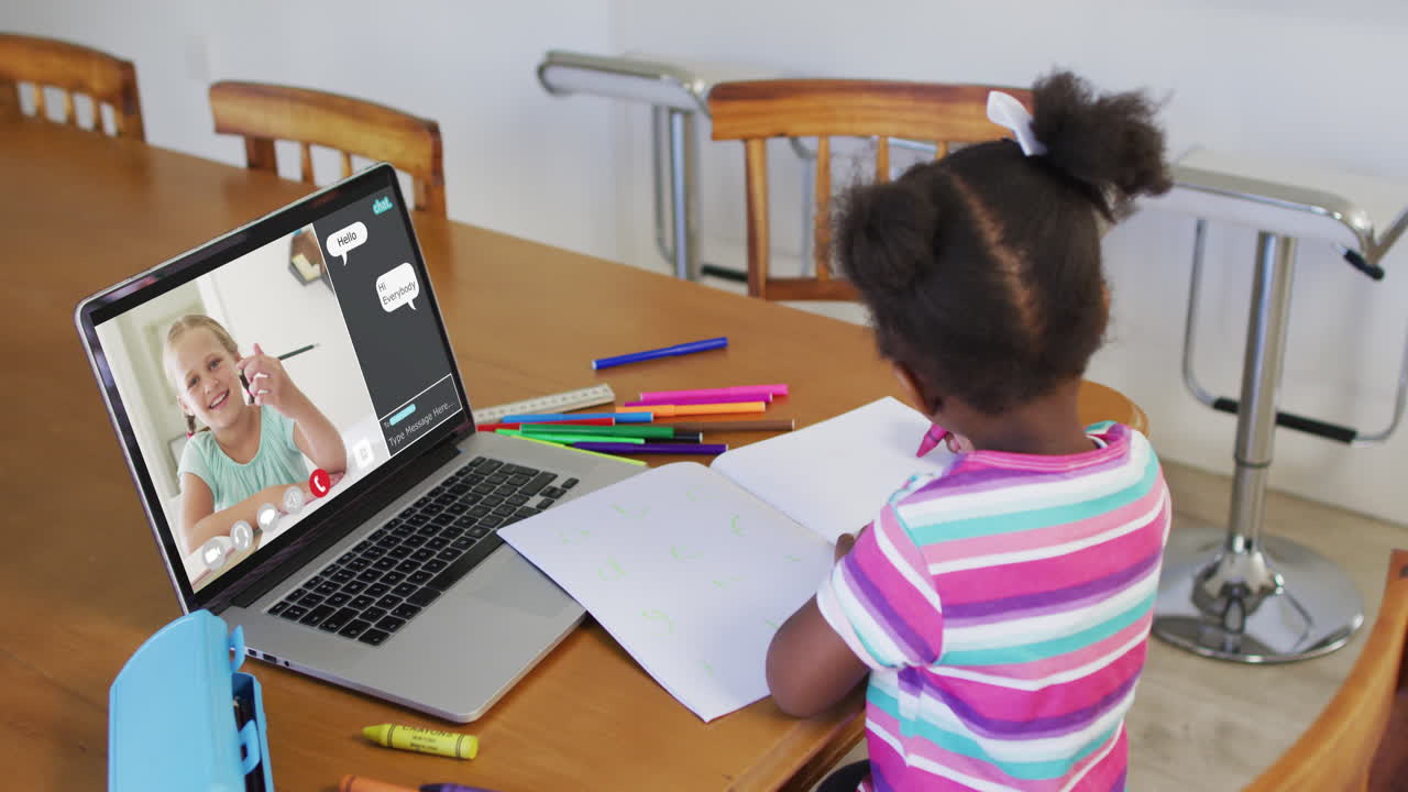 African american girl doing homework and having a video call with classmate on laptop at home