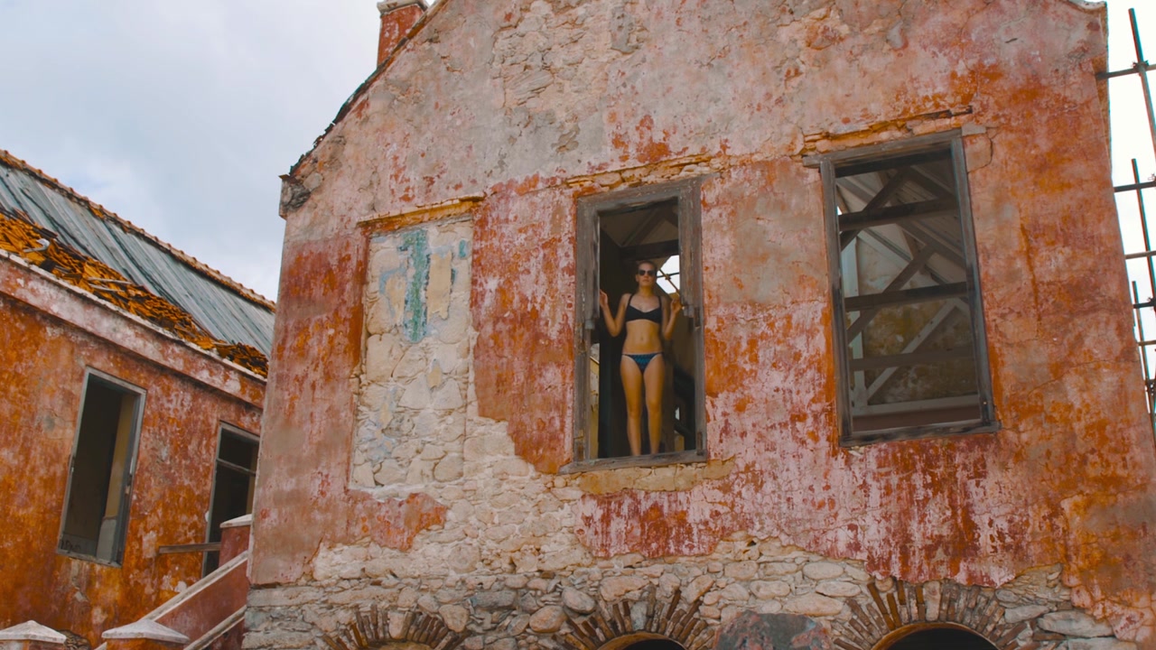 Ragazza in bikini in piedi nell'apertura di una finestra di un faro abbandonato