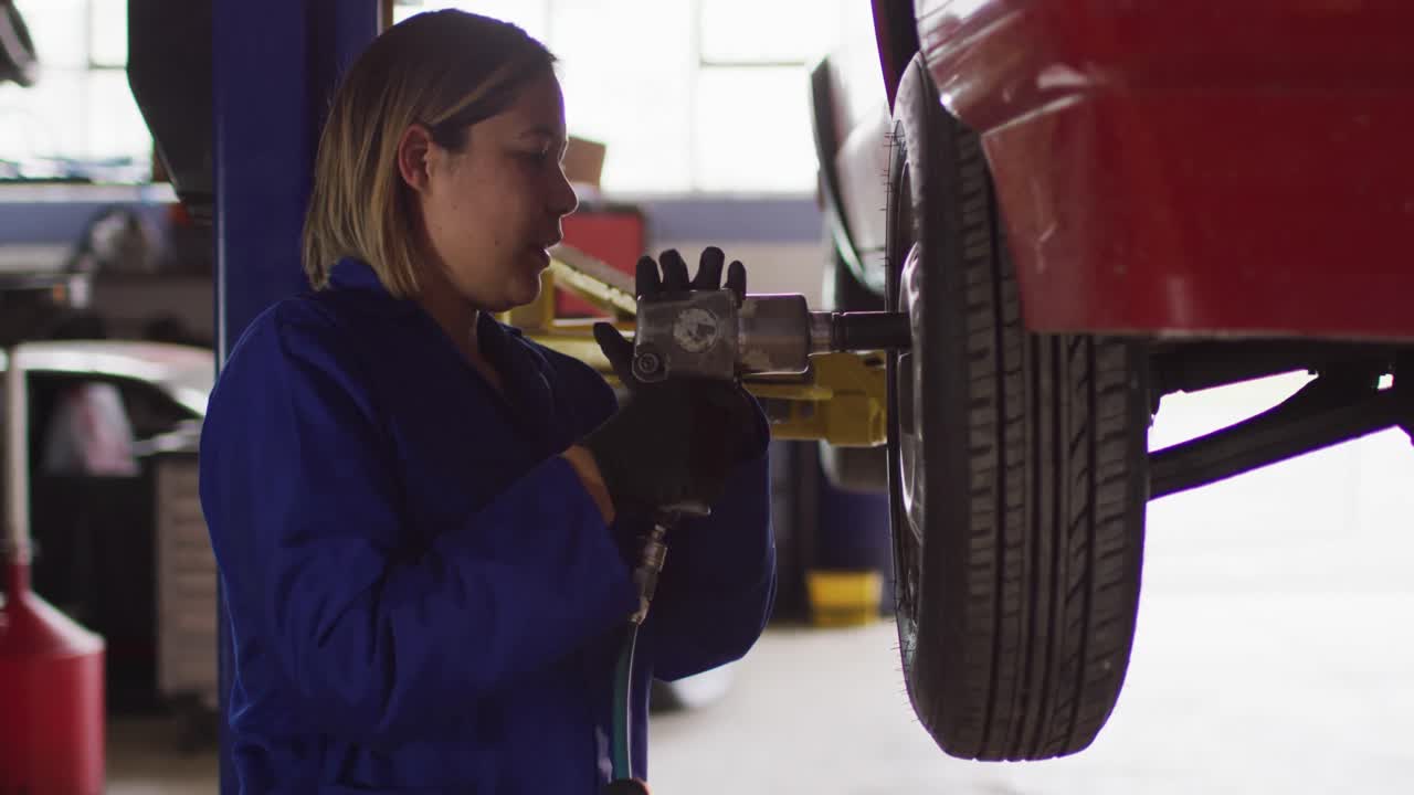 mecánica cambiando los neumáticos del automóvil usando un taladro eléctrico en una estación de servicio de automóviles