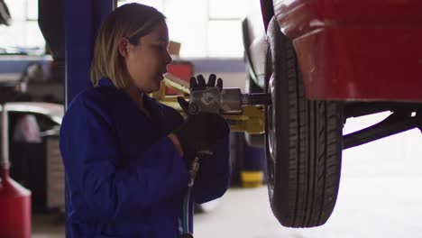 female mechanic changing tires of the car using power drill at a car service station