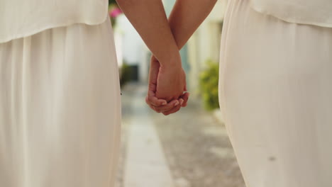 Close-up-of-an-unrecognizable-lesbian-brides-in-white-dresses-holding-hands-and-walking-together