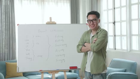 asian male teacher with glasses crossing arms and smiling to camera while teaching english at home