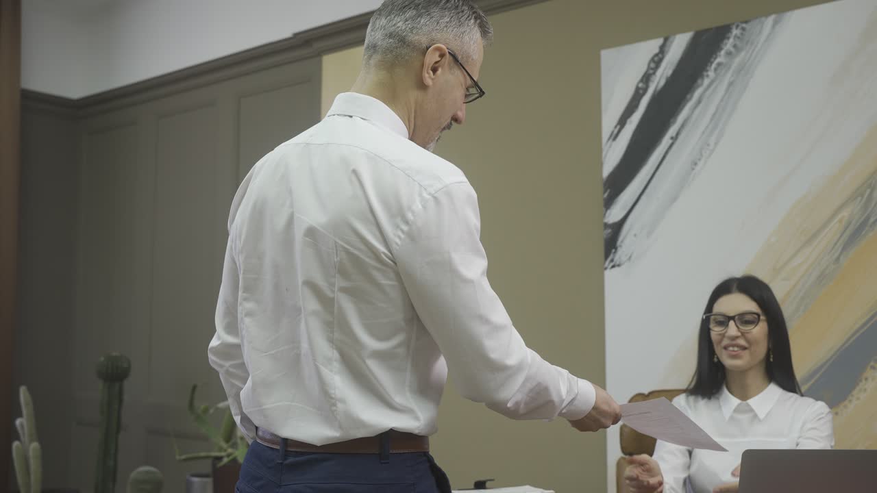 мужчина-служащий вручает документ своему начальнику, а затем они пожимают друг другу руки в офисе