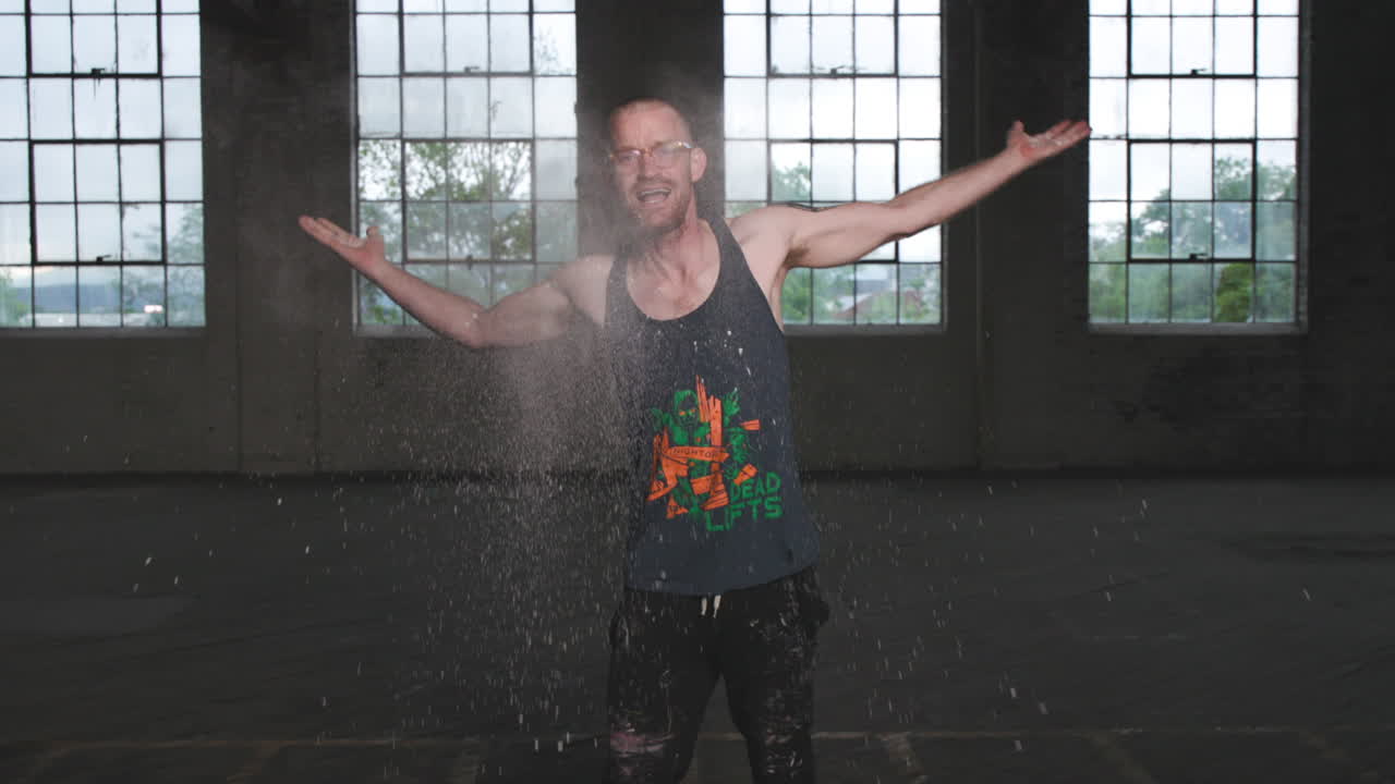 Slow motion footage of a man with flour in his hands dancing and yelling in an industrial setting.