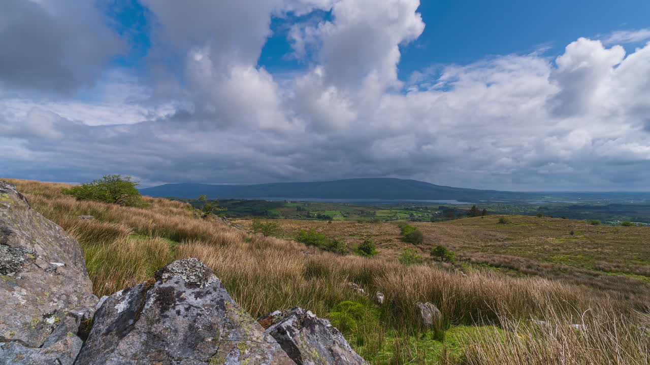 Time lapse of rural landscape with rocky foreground on hillside and lake in the distance on a cloudy sunny spring day in Arigna mountains in county Leitrim in Ireland
