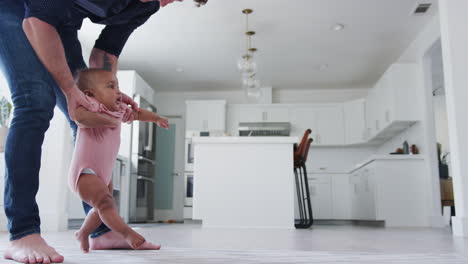 close up of father encouraging smiling baby daughter to take first steps and walk at home