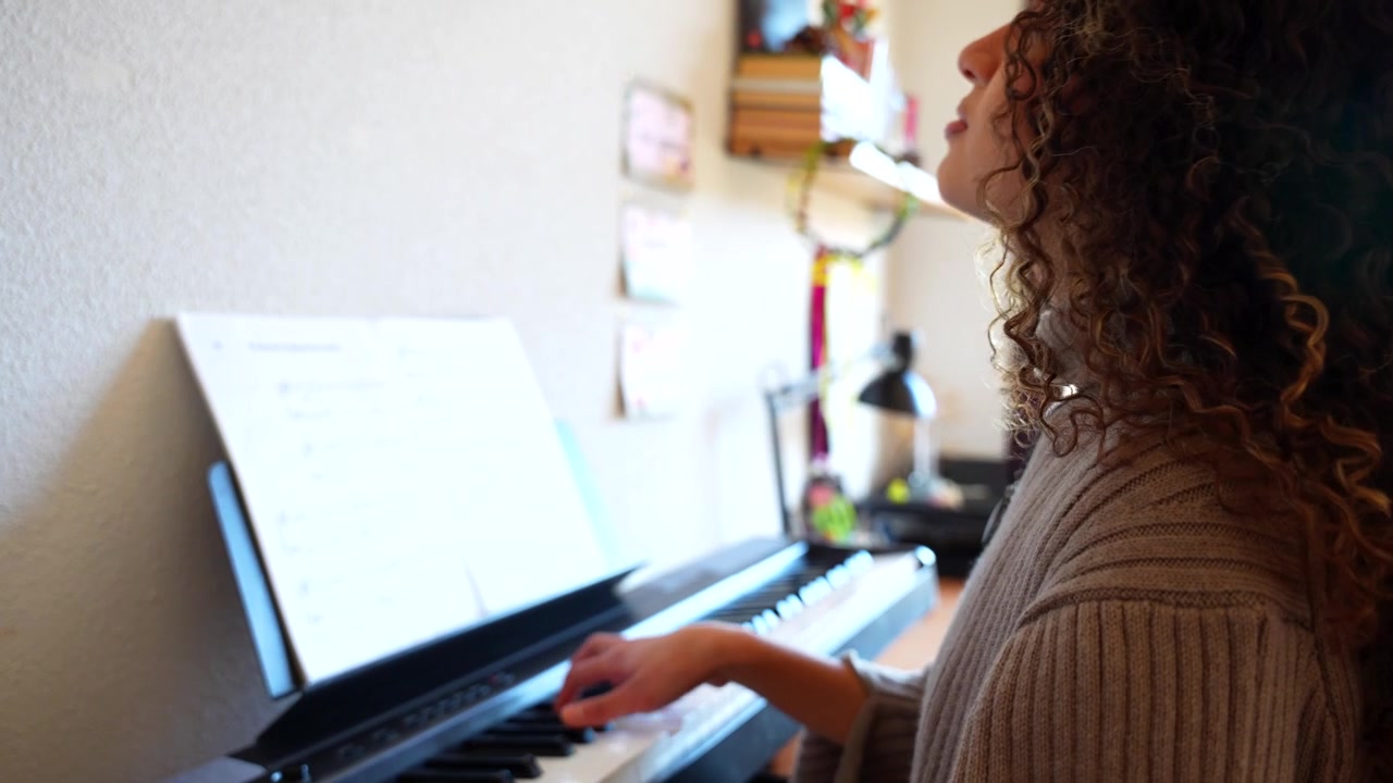Giovane musicista donna che si esercita al pianoforte elettrico leggendo uno spartito a casa