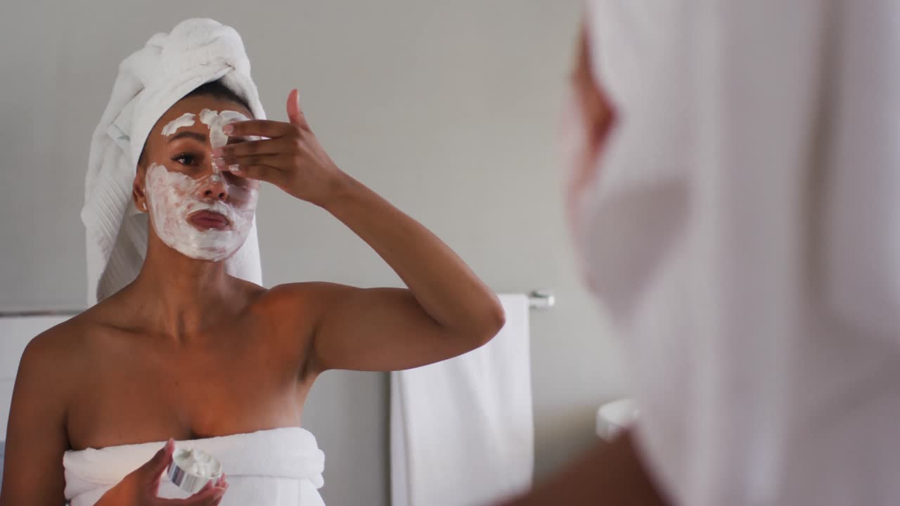 African american woman applying face mask looking in the mirror at bathroom