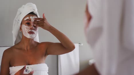 African-american-woman-applying-face-mask-looking-in-the-mirror-at-bathroom