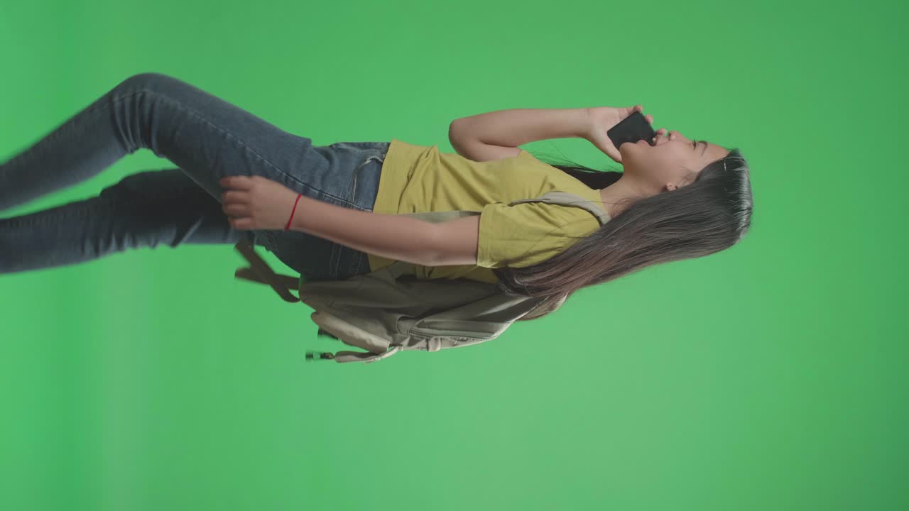 Side View Of Asian Girl Student Talking On Mobile Phone And Walking To School On Green Screen Chroma Key