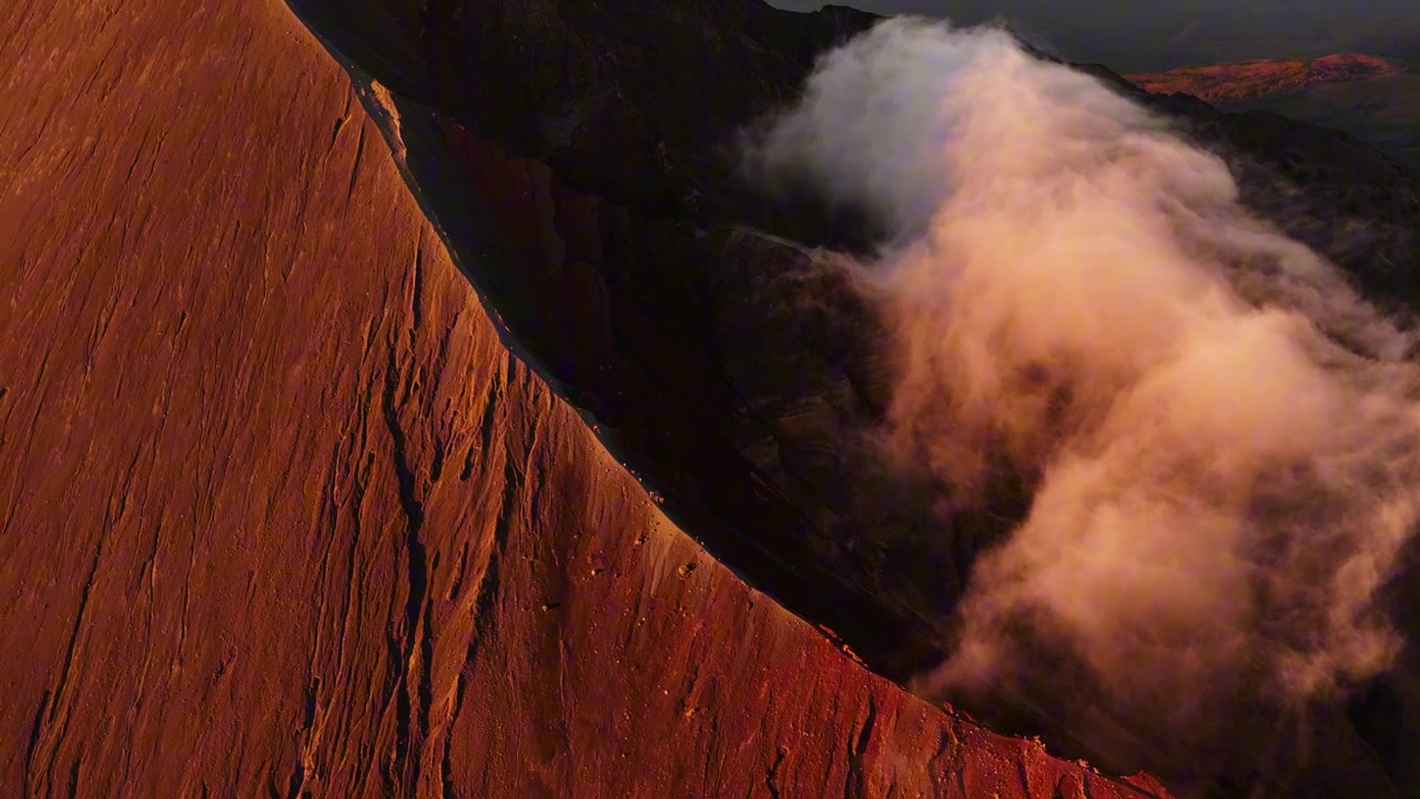 Ethereal cloud rising from volcanic crater beside steep illuminated slope, aerial orbit of heavenly landscape with stunning atmospheric glow