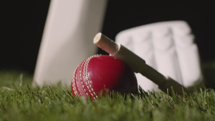Natura morta di cricket con primo piano di mazza, palla, bails e guanti adagiati sull'erba 4