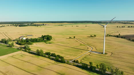 aerial view of a single wind turbine in an expansive agricultural landscape with a nearby road and small clusters of trees under a clear sky