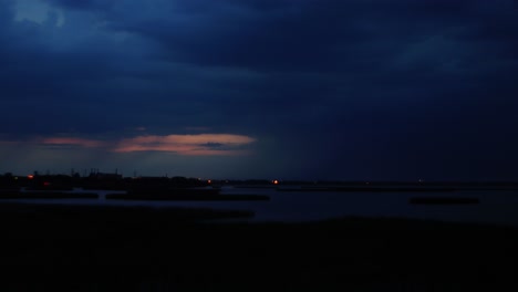 time lapse of dramatic dark thunderstorm clouds with lightning strikes rolling over the city and lake liepaja after the sunset, wide shot