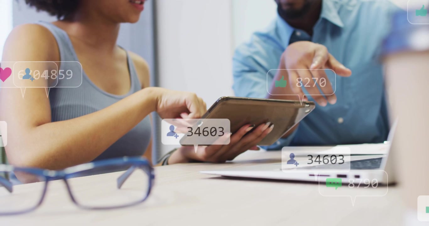 Woman tapping tablet and man pointing laptop starting marketing likes icons floating boosting reach