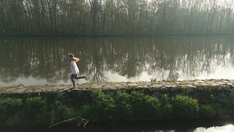 Chica-Con-Trenzas-Corriendo-En-Un-Muelle-De-Piedra-En-El-Río