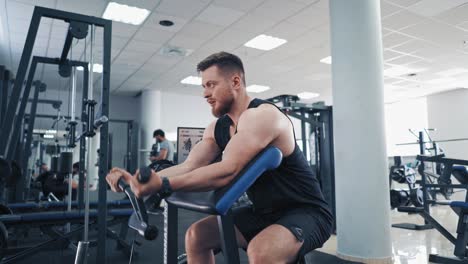 bearded man pumping his arm muscles in the gym. athletic bodybuilder training his biceps on a modern simulator and looking confidently forward.