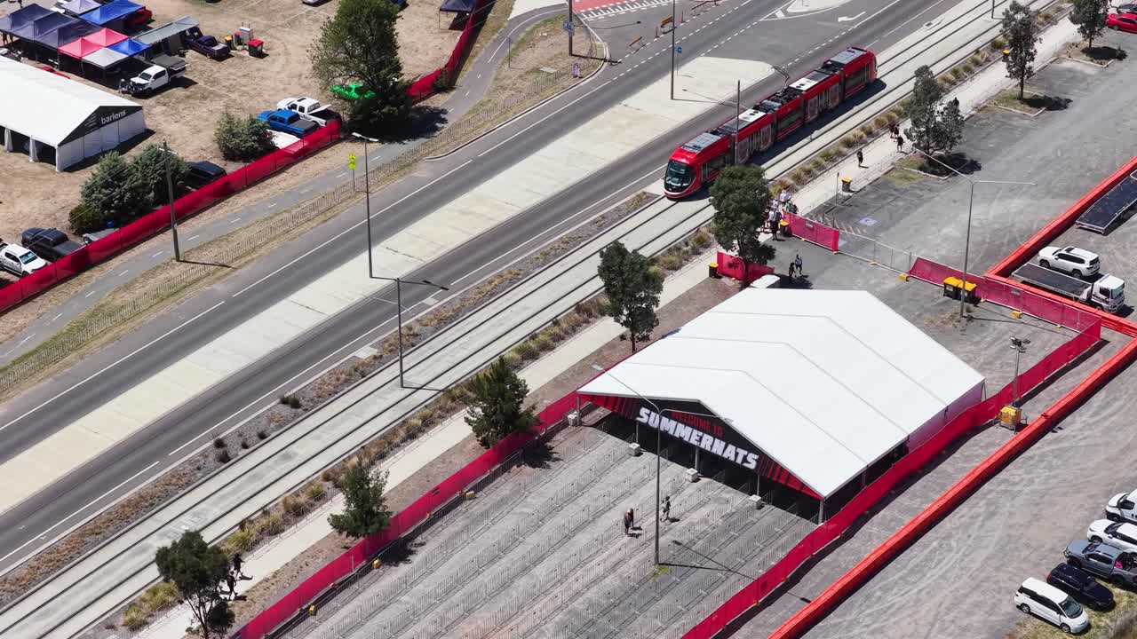 Ripresa aerea dall'alto di un tram rosso che passa davanti a un grande tendone bianco per eventi